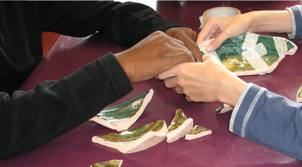 Atelier remontage de poteries ©ADVCBRIE Mains de personnes en train de reconstituer une poterie. 